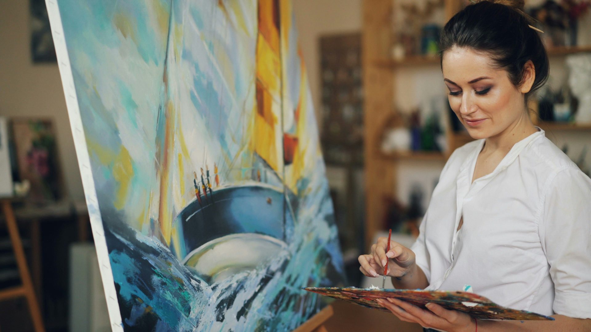 A woman paints a sailboat on a canvas.